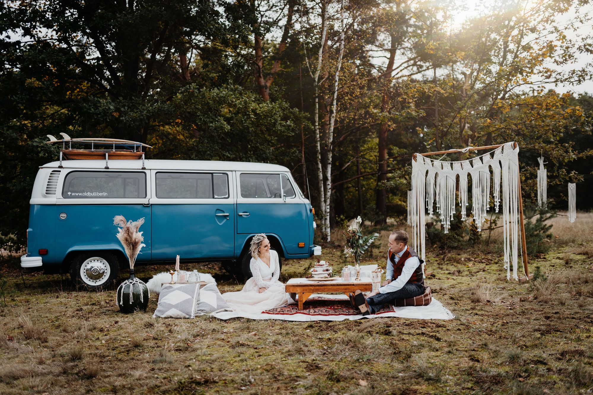 Ein Paar sitzt auf einer Decke neben einem VW-Bus.