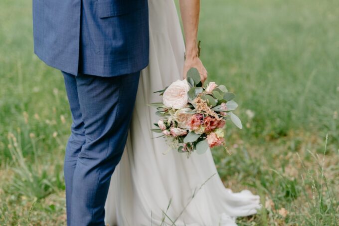 Eine Braut und ein Bräutigam stehen auf einem Feld und halten ihre Blumensträuße in der Hand.