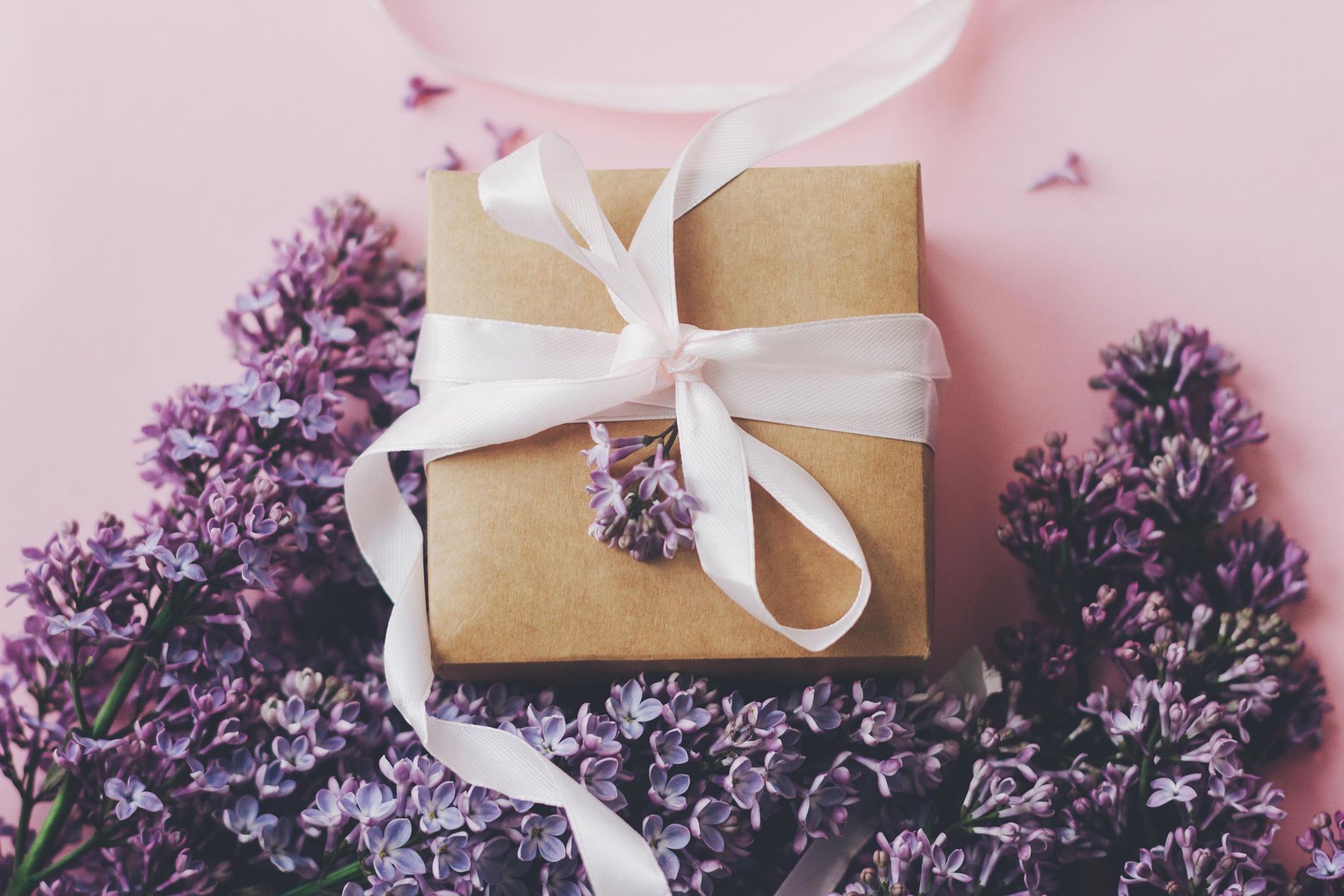 Eine Geschenkbox mit lila Blumen auf rosa Hintergrund.