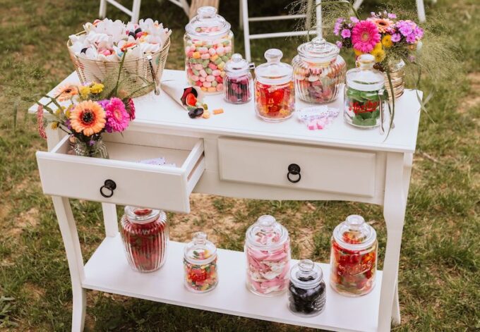 Ein weißer Tisch mit Gläsern voller Süßigkeiten und Blumen.