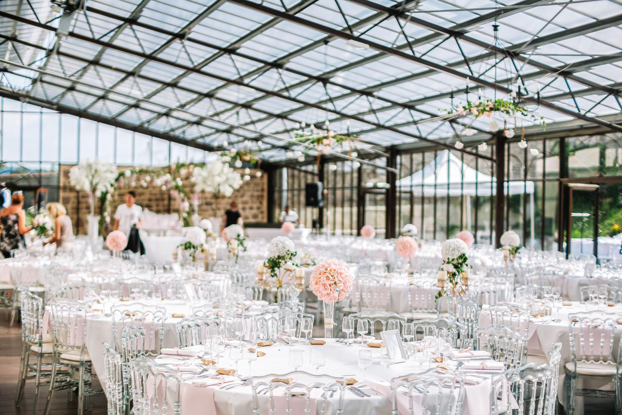 Ein Hochzeitsempfang in einem Gewächshaus mit weißen Tischen und Stühlen.