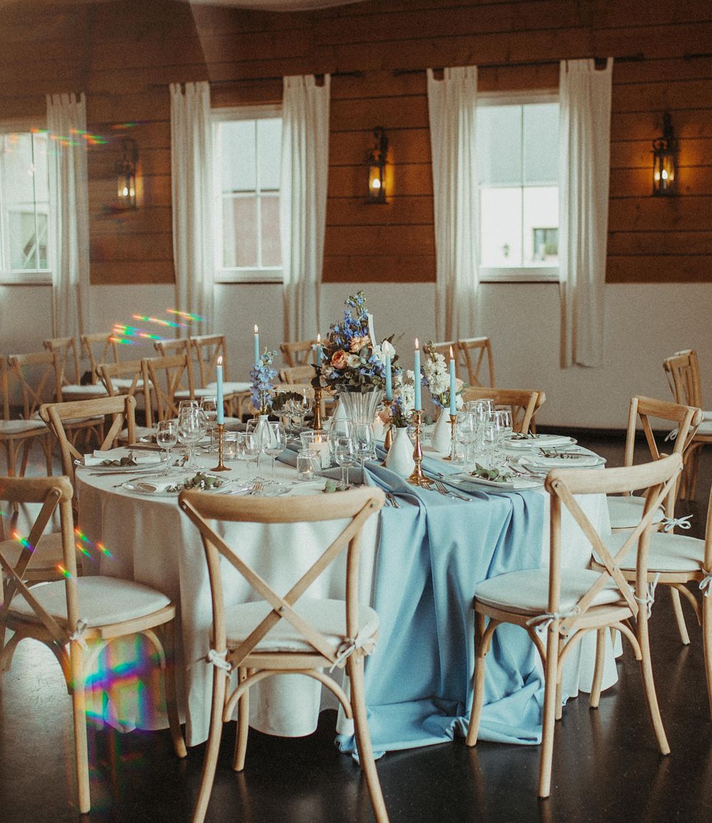 Ein Hochzeitsempfang mit blauer Bettwäsche und weißen Stühlen.
