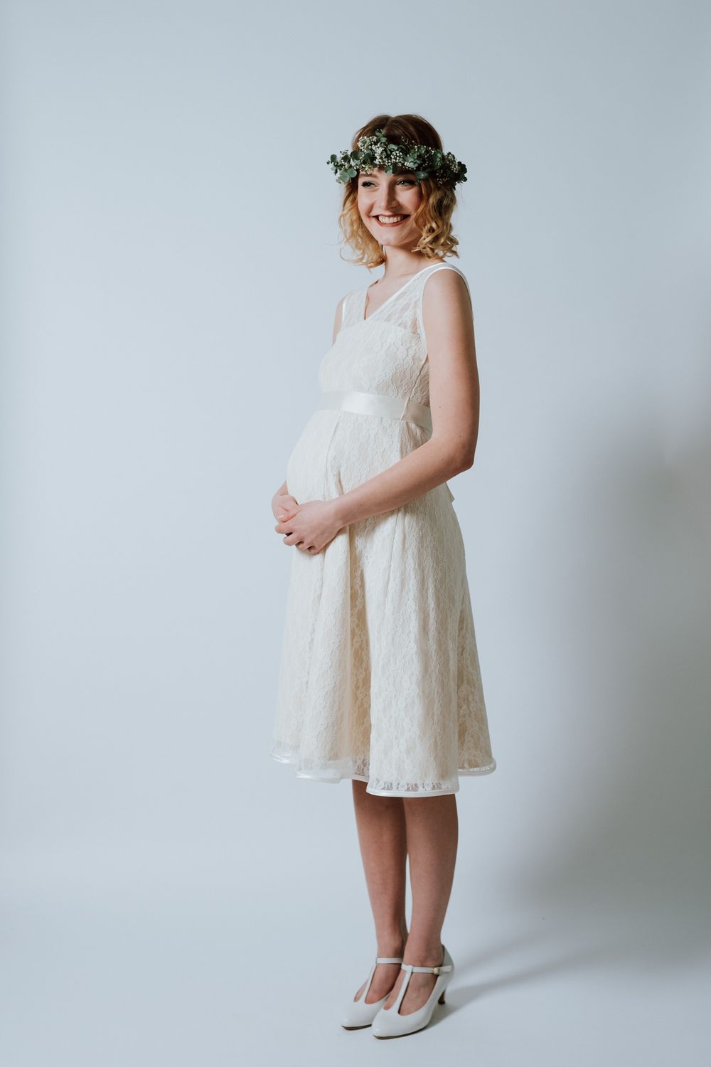 Eine schwangere Frau in einem weißen Kleid posiert für ein Foto.