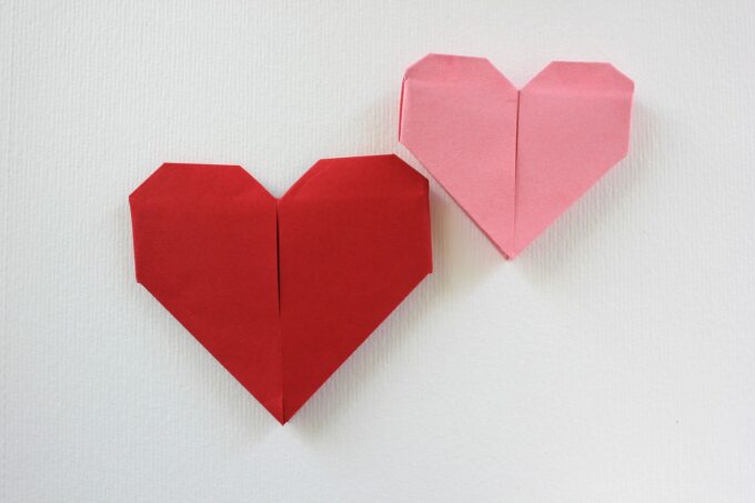 Zwei Origami-Herzen auf einer weißen Wand.