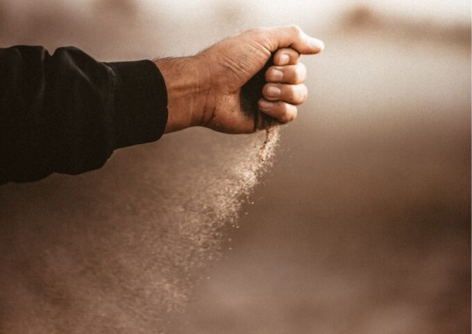 Die Hand eines Mannes wirft Sand in die Luft.