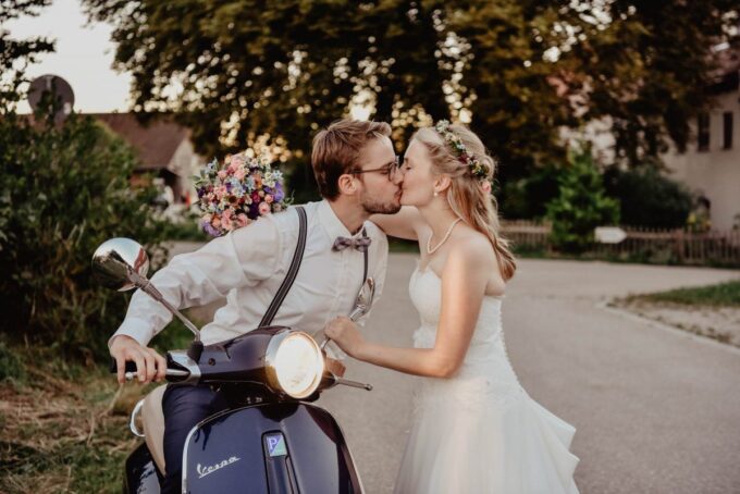 Eine Braut und ein Bräutigam küssen sich auf einer Vespa.
