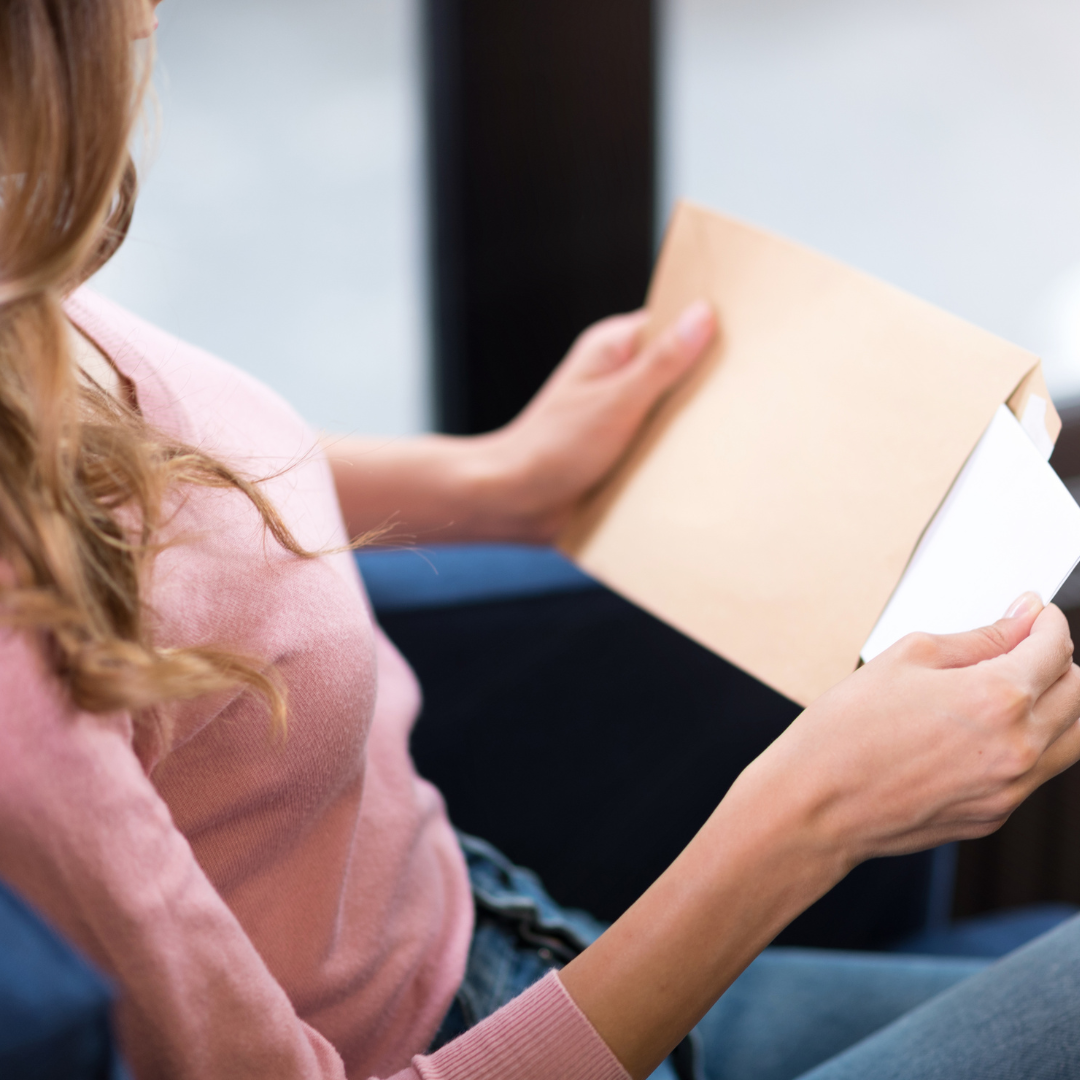 Eine Frau sitzt auf einer Couch und hält einen Umschlag.