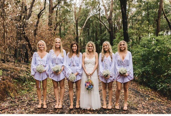 Eine Gruppe Brautjungfern in lavendelfarbenen Gewändern steht im Wald.