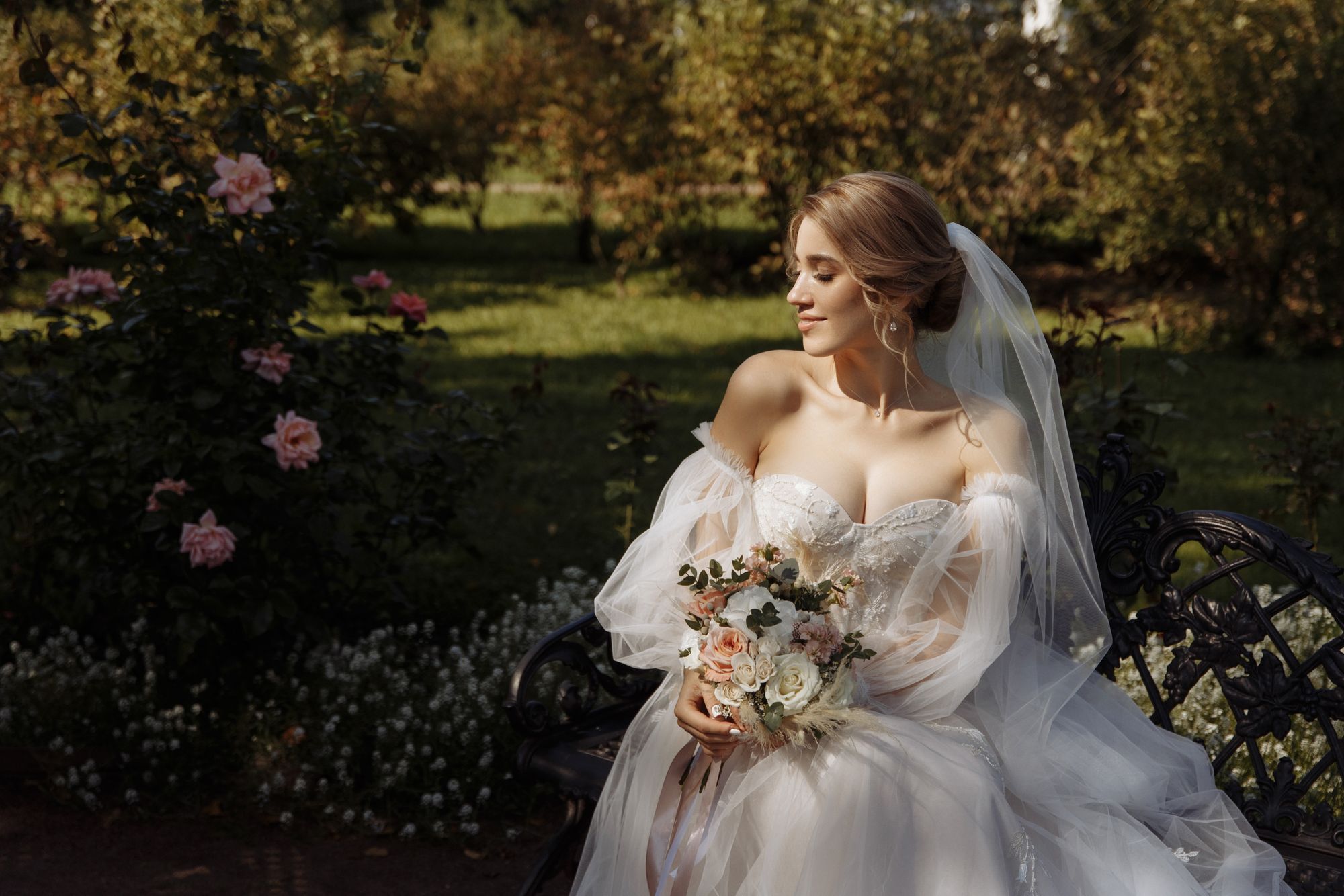 Eine schöne Braut in einem Hochzeitskleid sitzt auf einer Bank in einem Park.