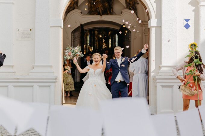 Eine Braut und ein Bräutigam verlassen mit Papierkonfetti eine Kirche.
