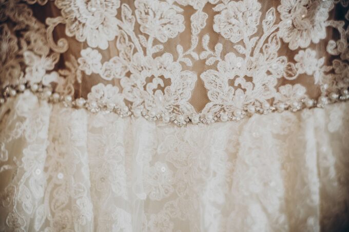 Eine Nahaufnahme eines Hochzeitskleides mit Spitze und Perlen.