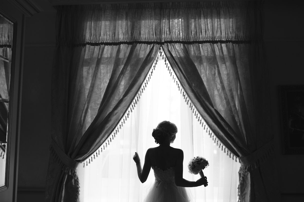 Eine Braut in einem Hochzeitskleid steht vor einem Fenster.