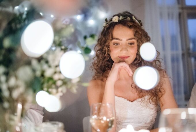 Eine Braut sitzt an einem Tisch mit Lichtern um sie herum.
