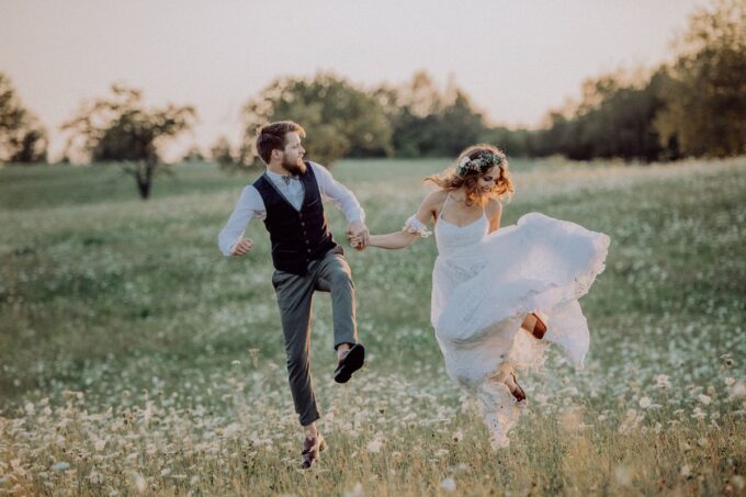 Braut und Bräutigam springen bei Sonnenuntergang auf einem Feld.