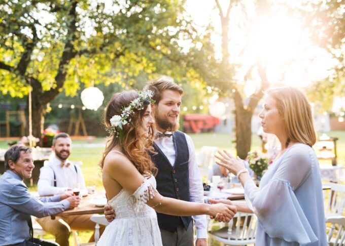 Eine Braut und ein Bräutigam schütteln sich bei einem Hochzeitsempfang im Freien die Hand.
