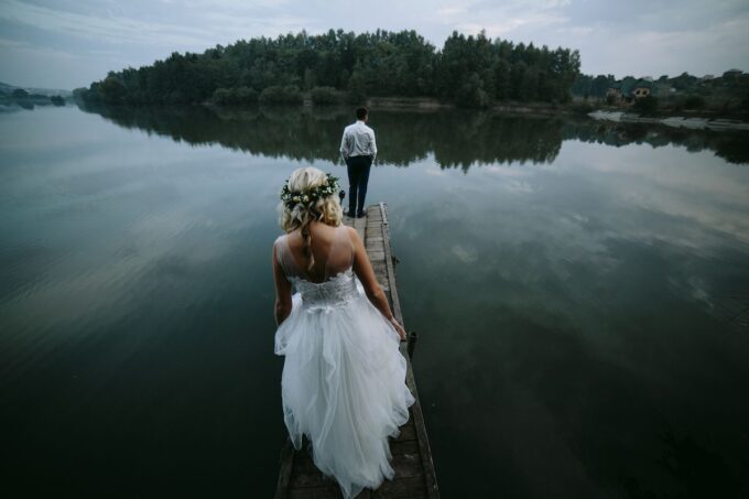 Eine Braut und ein Bräutigam stehen auf einem Steg in der Nähe eines Sees.