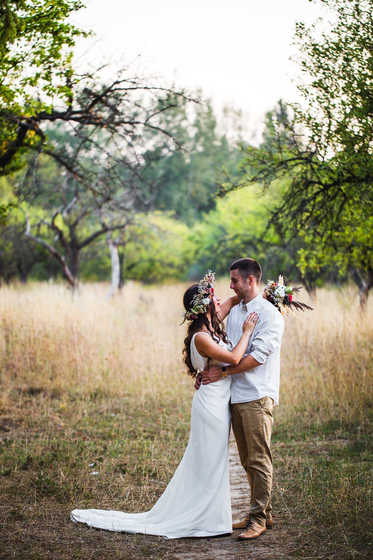 Eine Braut und ein Bräutigam küssen sich mitten in einem Obstgarten.