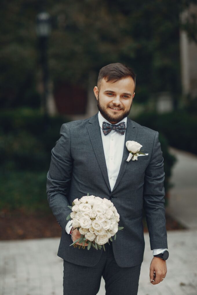 Ein Bräutigam im grauen Anzug hält einen Blumenstrauß.