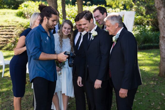 Eine Gruppe von Menschen blickt vor einem Brautpaar in eine Kamera.