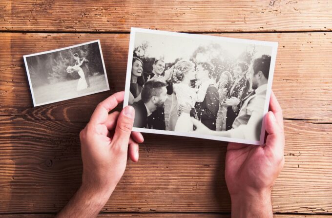 Hände halten ein Foto einer Hochzeit auf einem Holztisch.