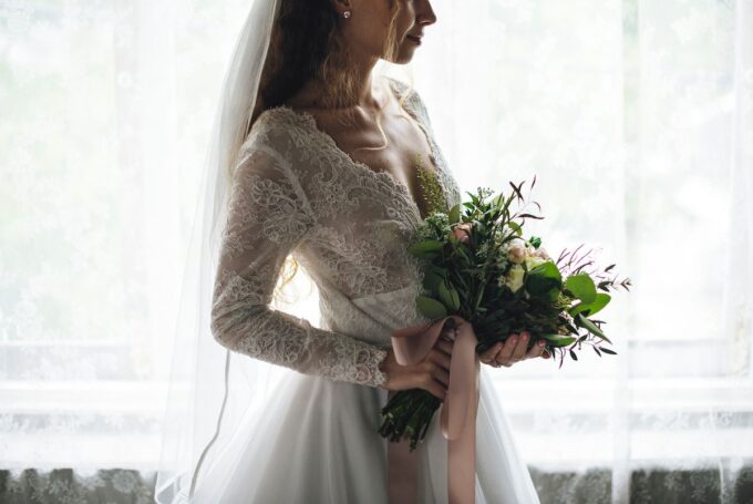 Eine Braut in einem Hochzeitskleid steht am Fenster.