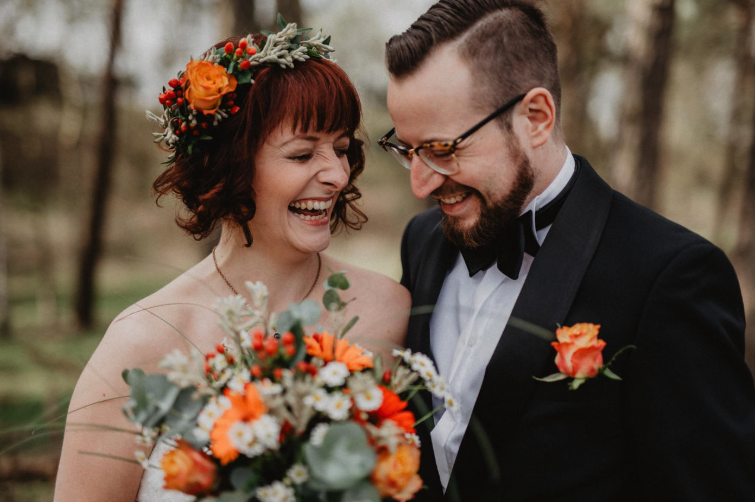 Eine Braut und ein Bräutigam lachen im Wald.