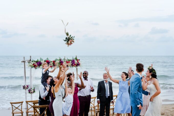 Eine Hochzeitszeremonie am Strand, bei der Menschen Blumen in die Luft werfen.