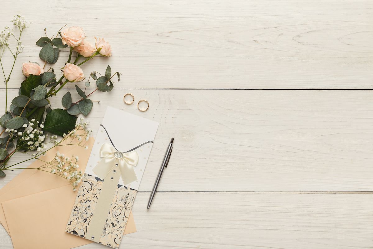 Eine Hochzeitseinladung mit Rosen und einem Umschlag auf einem weißen Holztisch.