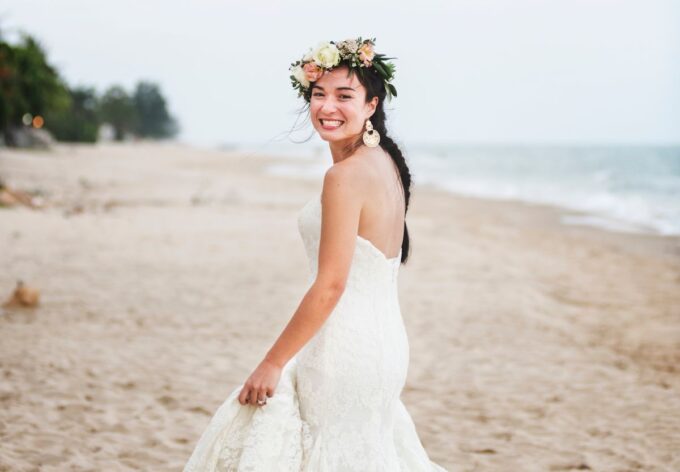 Eine Braut in einem weißen Hochzeitskleid geht am Strand spazieren.