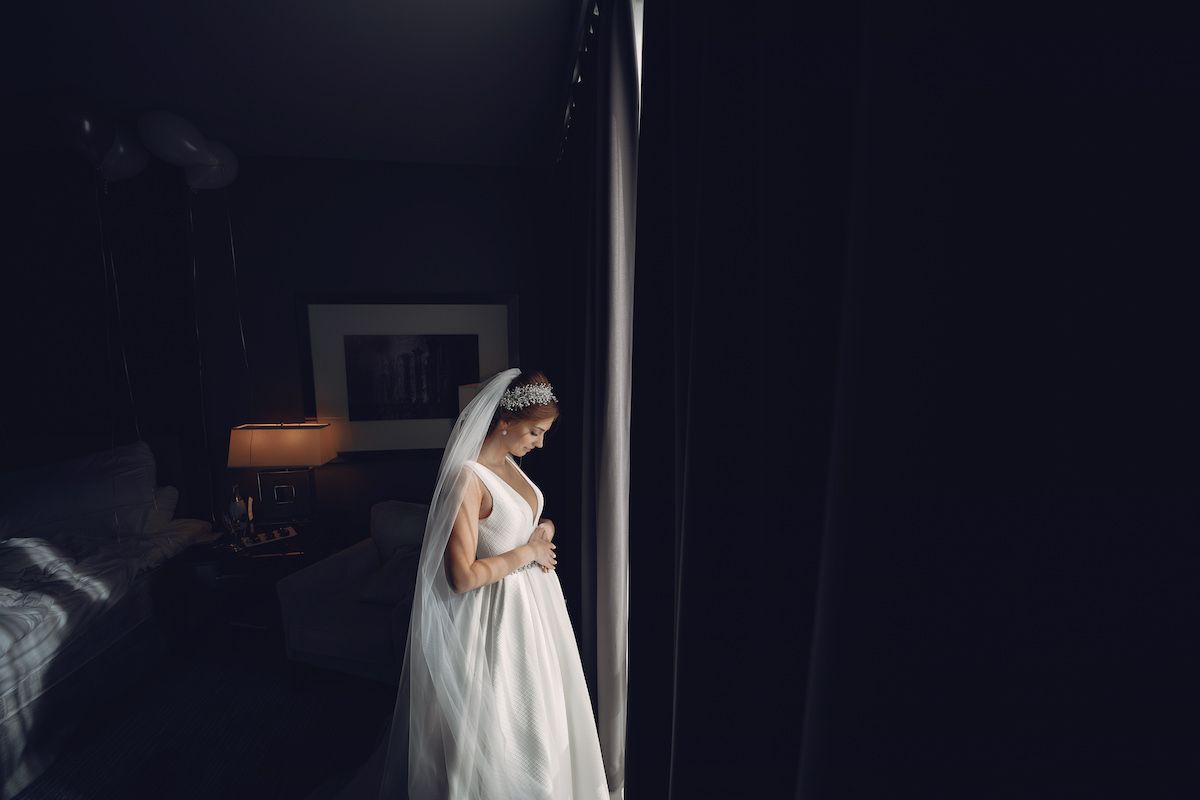 Eine Braut in einem Hochzeitskleid steht vor einem Fenster.