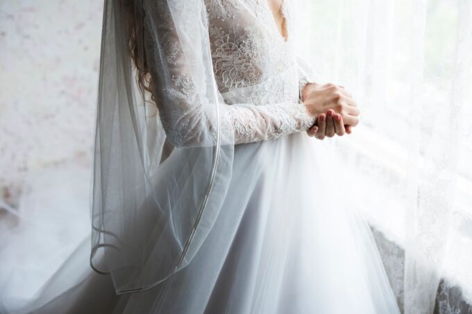 Eine Braut in einem weißen Hochzeitskleid steht am Fenster.