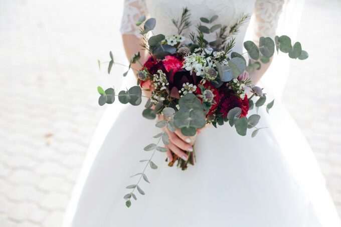 Eine Braut hält einen Strauß Eukalyptus und rote Rosen.