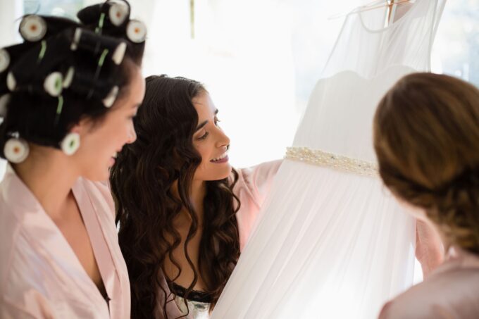 Drei Brautjungfern betrachten ein Hochzeitskleid.