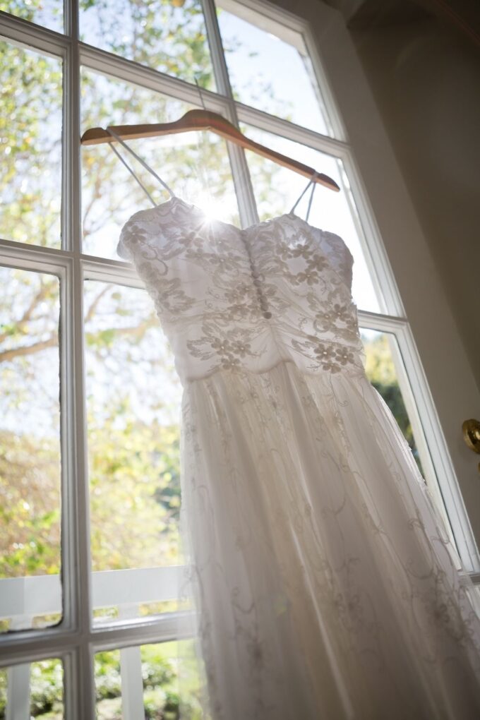 Vor einem Fenster hängt ein Hochzeitskleid.