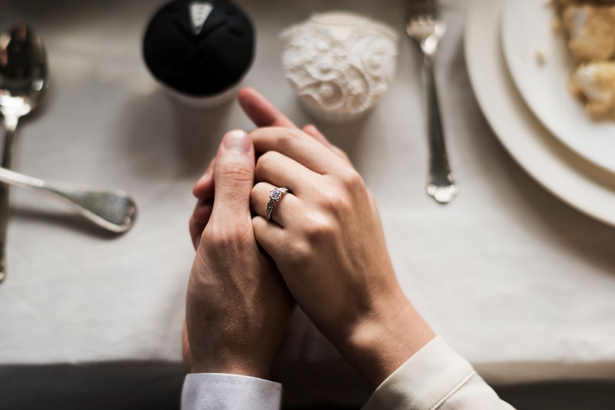 Ein Paar hält Händchen mit einem Ehering an einem Tisch.