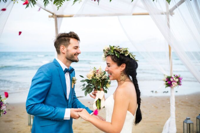 Eine Braut und ein Bräutigam stehen unter einem Hochzeitsbogen am Strand.