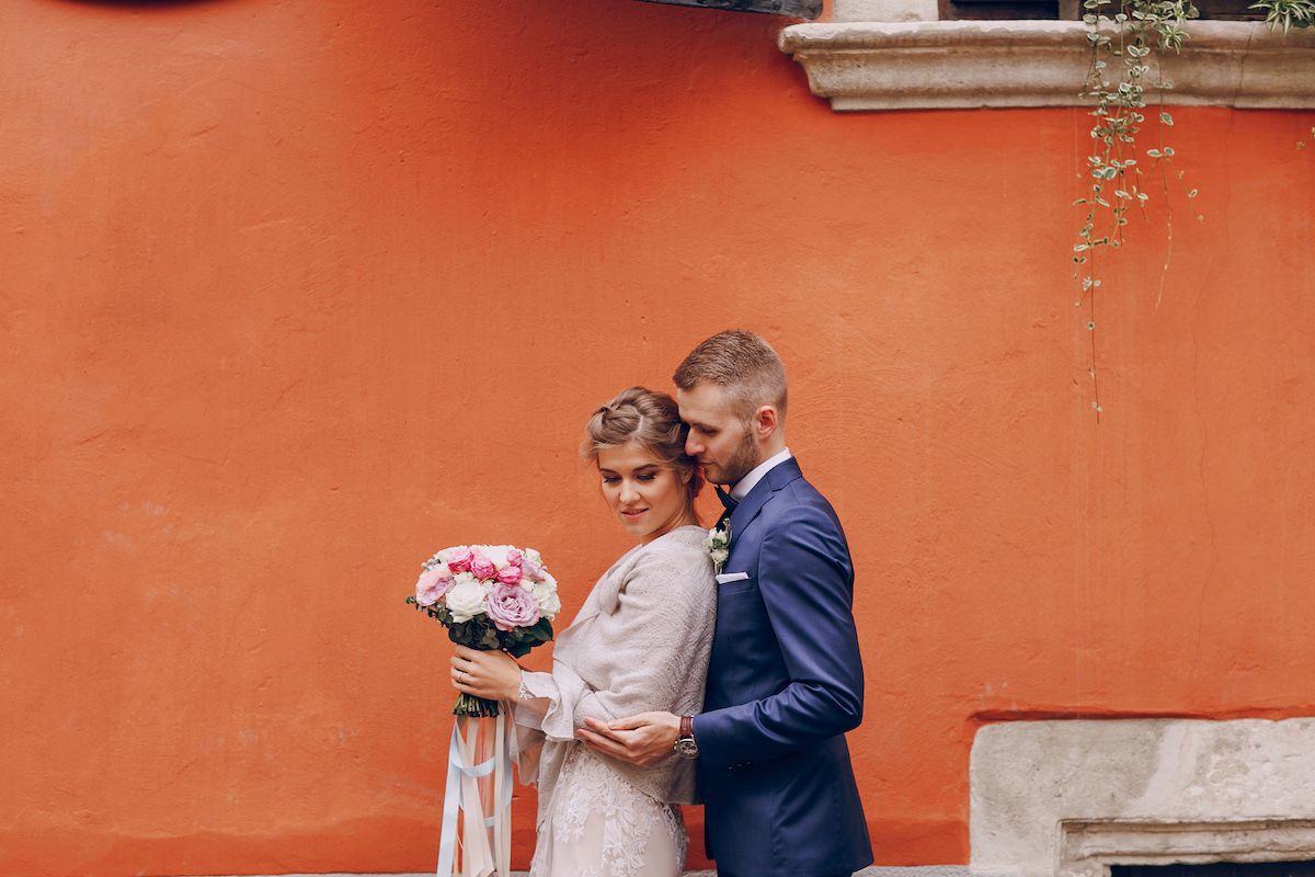 Eine Braut und ein Bräutigam posieren vor einer orangefarbenen Wand.