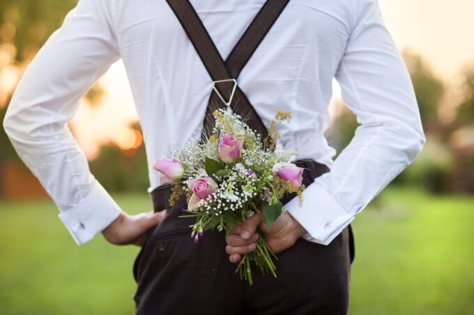 Ein Mann mit Hosenträgern hält einen Blumenstrauß in der Hand.