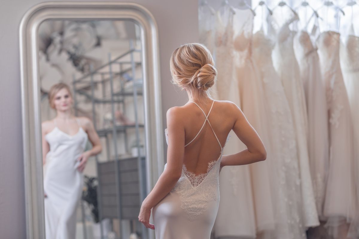Eine Frau in einem Hochzeitskleid, die sich im Spiegel betrachtet.