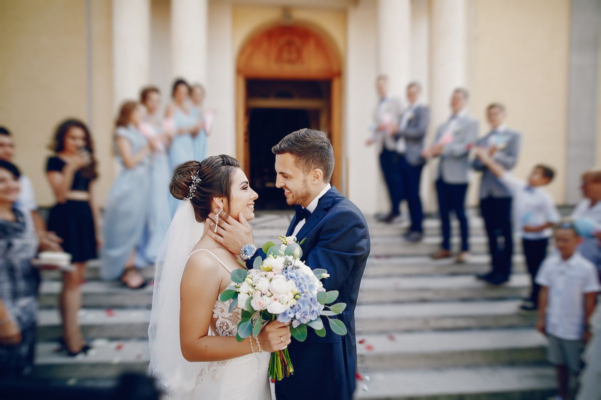 Eine Braut und ein Bräutigam küssen sich auf den Stufen einer Kirche.