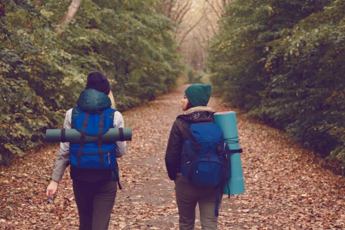 Zwei Personen mit Rucksäcken gehen einen Pfad im Wald entlang.