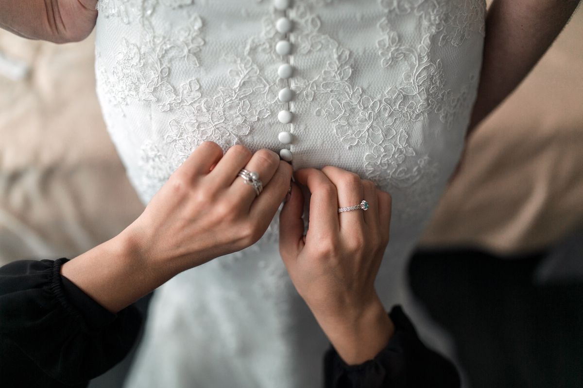 Eine Frau steckt ihren Ehering an das Kleid einer Braut.