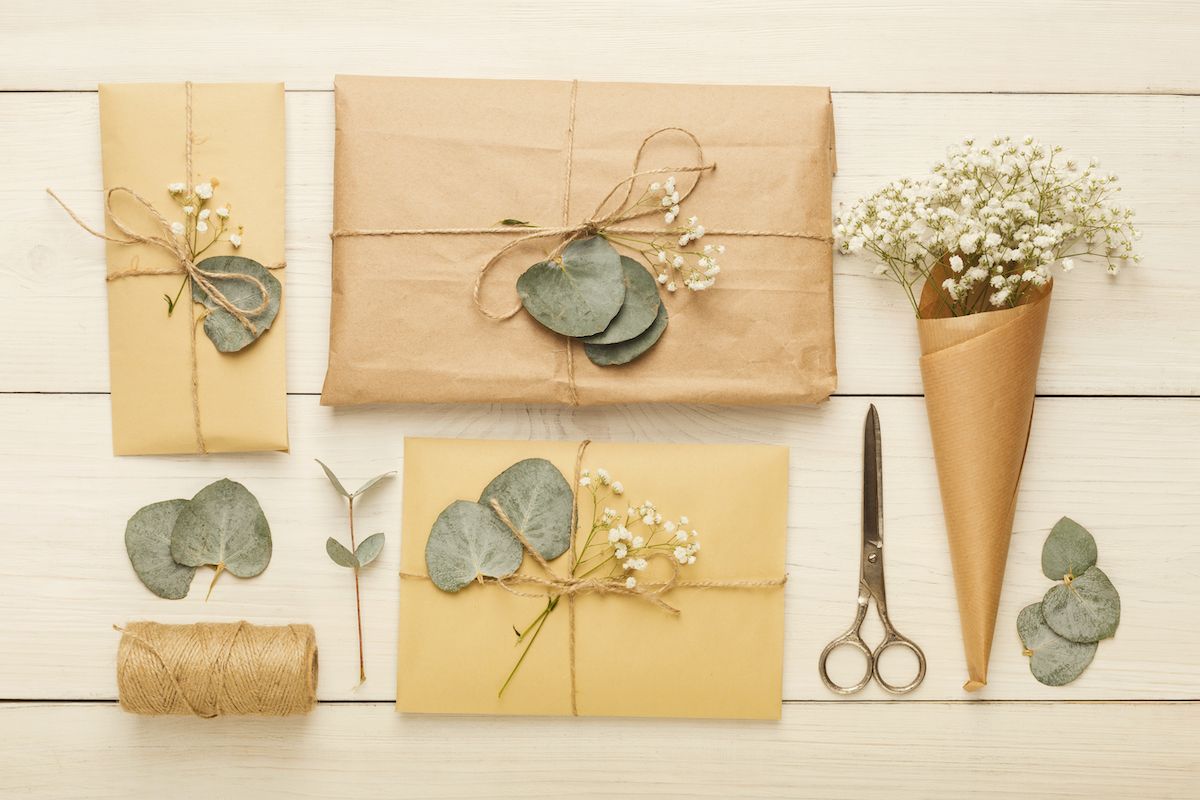 Geschenkpapier, Schere und Eukalyptusblätter auf einem Holztisch.