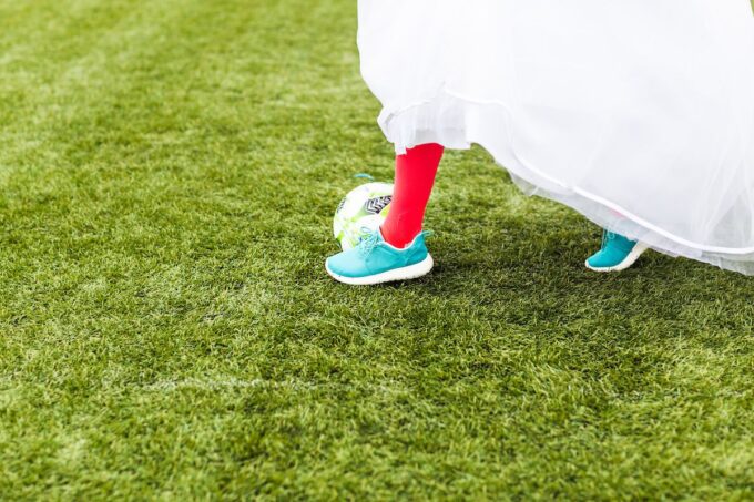 Eine Braut in einem Hochzeitskleid läuft mit einem Fußball über Gras.