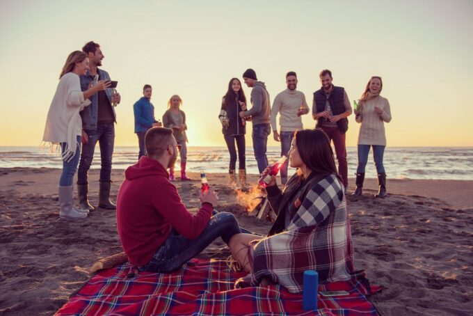 Eine Gruppe von Freunden sitzt am Lagerfeuer am Strand.