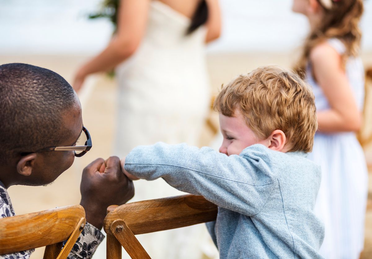 Ein kleiner Junge berührt bei einer Strandhochzeit die Hand eines Mannes.