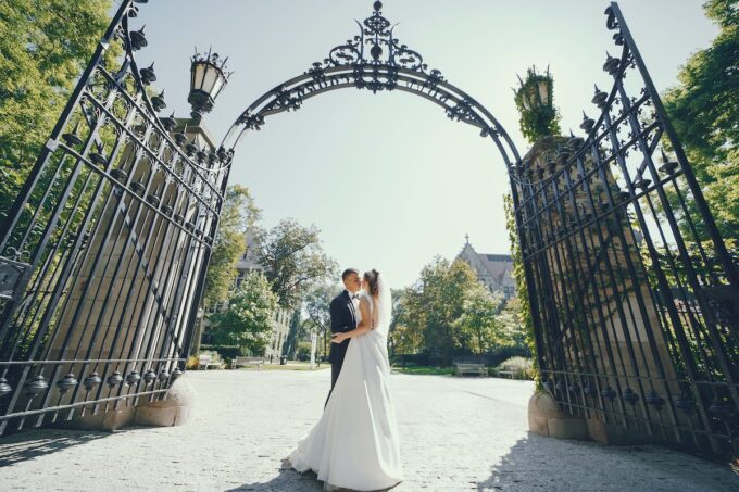 Eine Braut und ein Bräutigam küssen sich vor einem Eisentor.