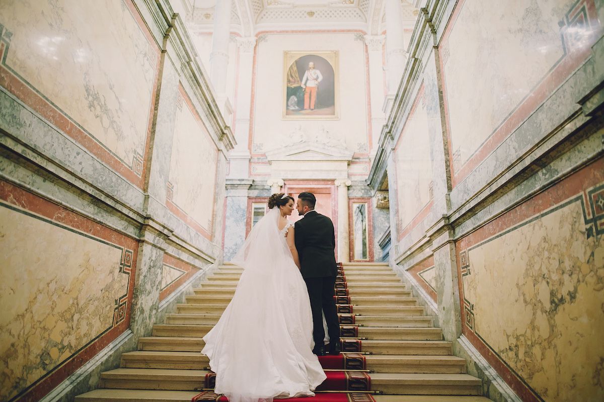 Eine Braut und ein Bräutigam stehen auf der Treppe eines reich verzierten Gebäudes.