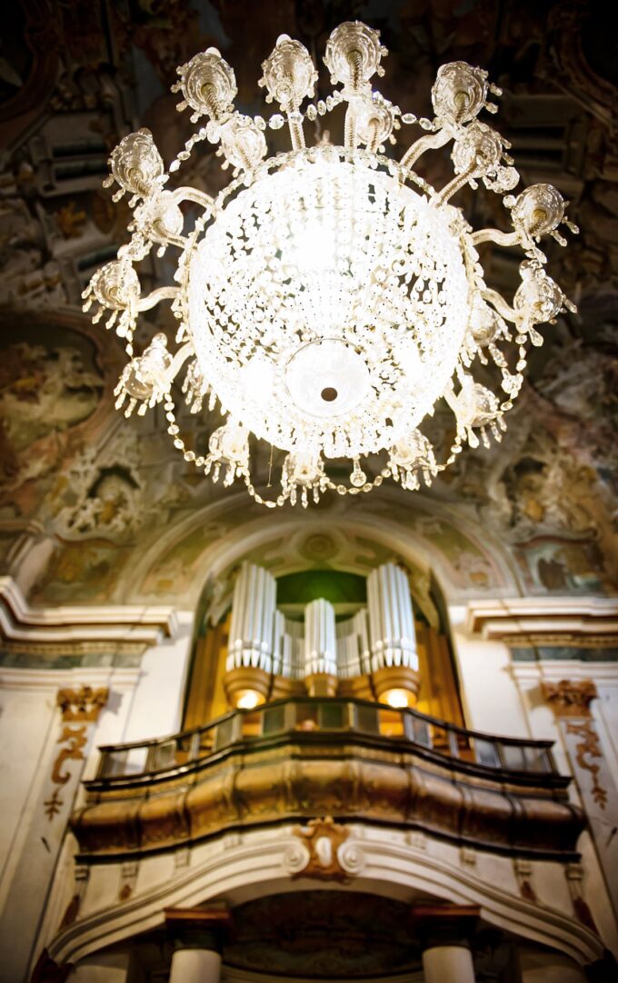 Über einer Orgel in einer Kirche hängt ein reich verzierter Kronleuchter.