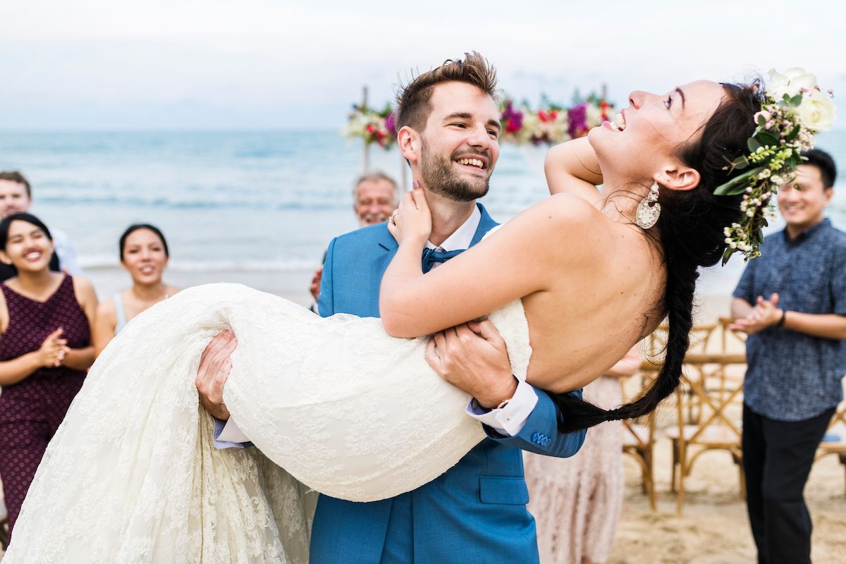 Eine Braut und ein Bräutigam werden während ihrer Hochzeitszeremonie am Strand getragen.